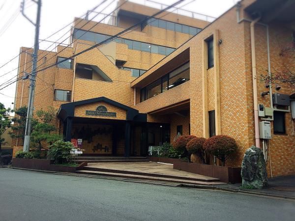 レンガ調の外壁が印象的な建物。玄関部分には屋根が付き、周辺にはたくさんの木が植えられている。