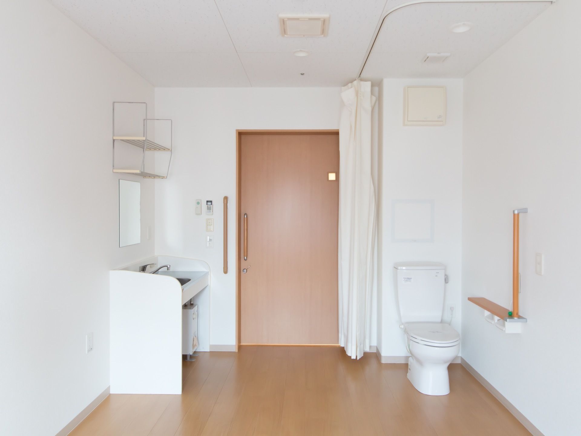 フローリングの床で白い壁の居室である。入口より入ると右手に洗面台があり、左手にはトイレがある。洗面台の上に棚がある。