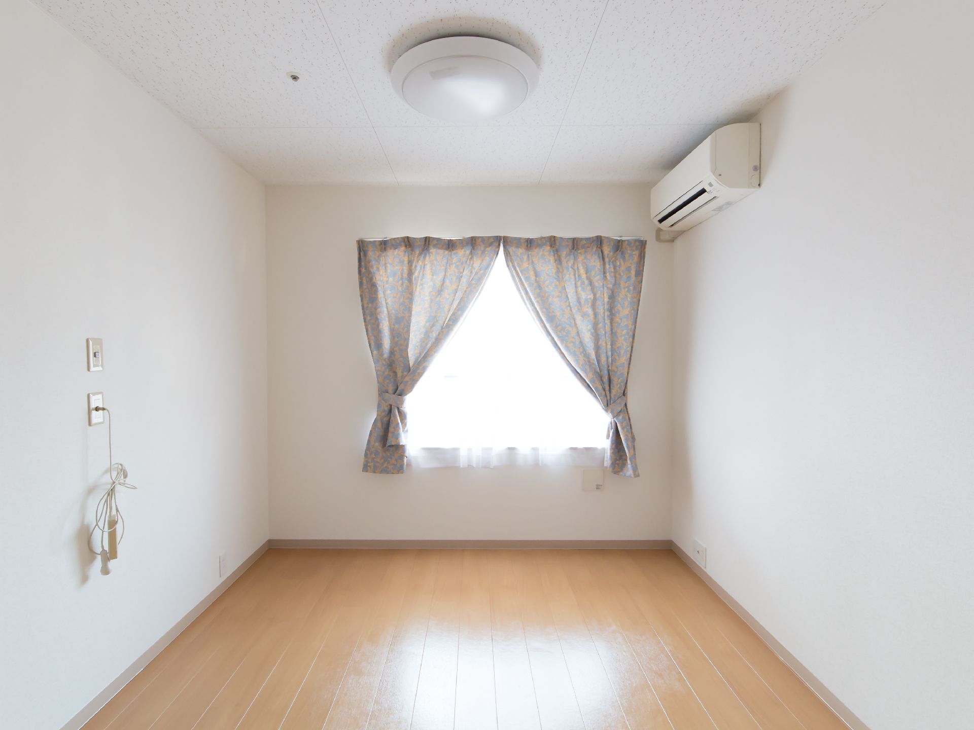 木目調のフローリングで白い壁にエアコンや窓が設置されたご入居前の居室