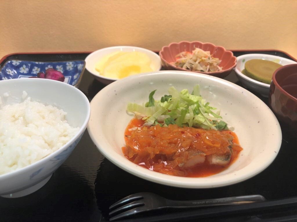 ソースがたっぷりかかったメインの肉料理にはサラダが添えられ、その周りには漬物やご飯、汁物、野菜の和え物などが並んでいる。