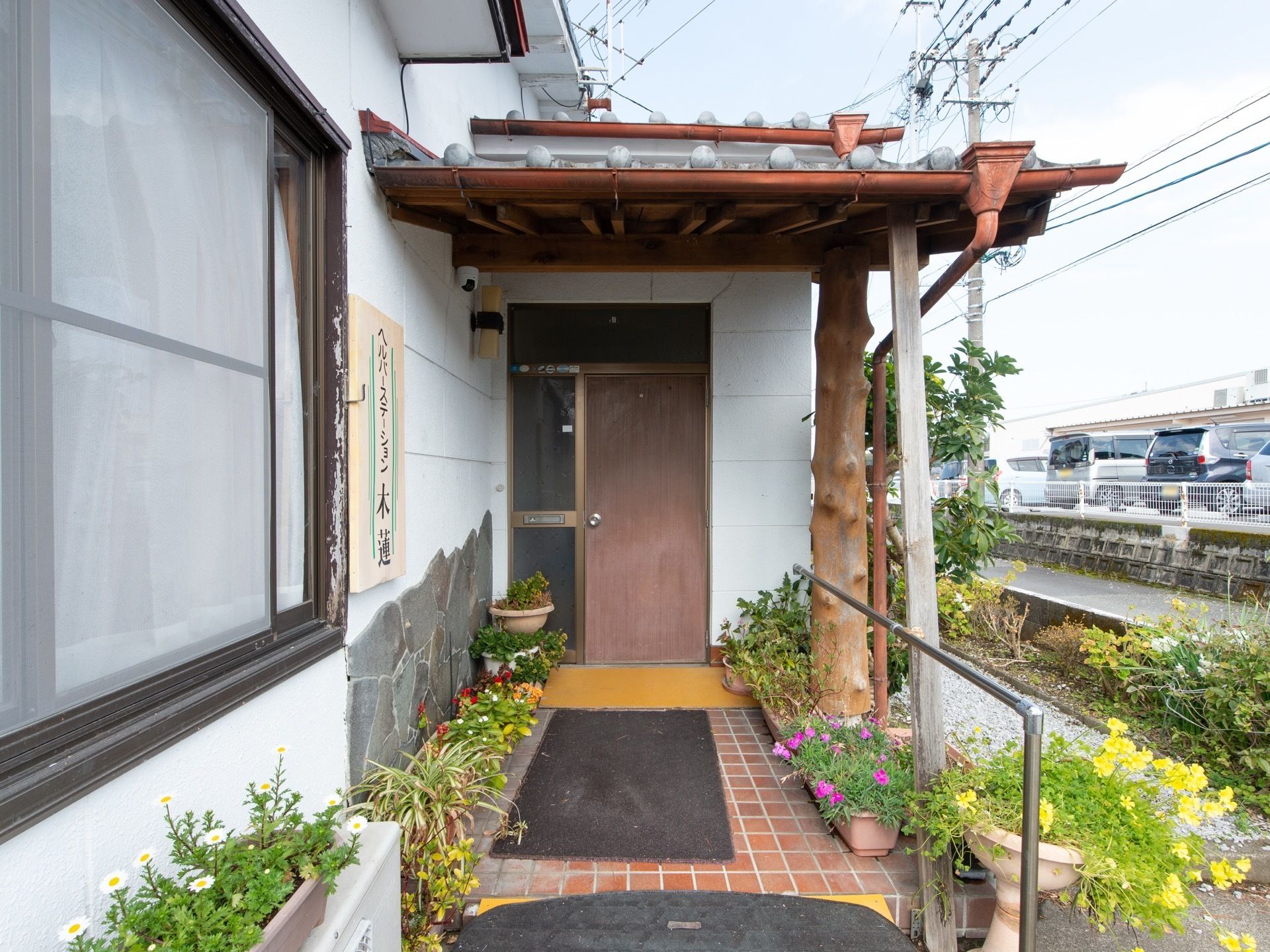 施設玄関は、馴染みある住宅玄関のような面持ちである。両サイドには、植木鉢に植えられた草花が並べられている。