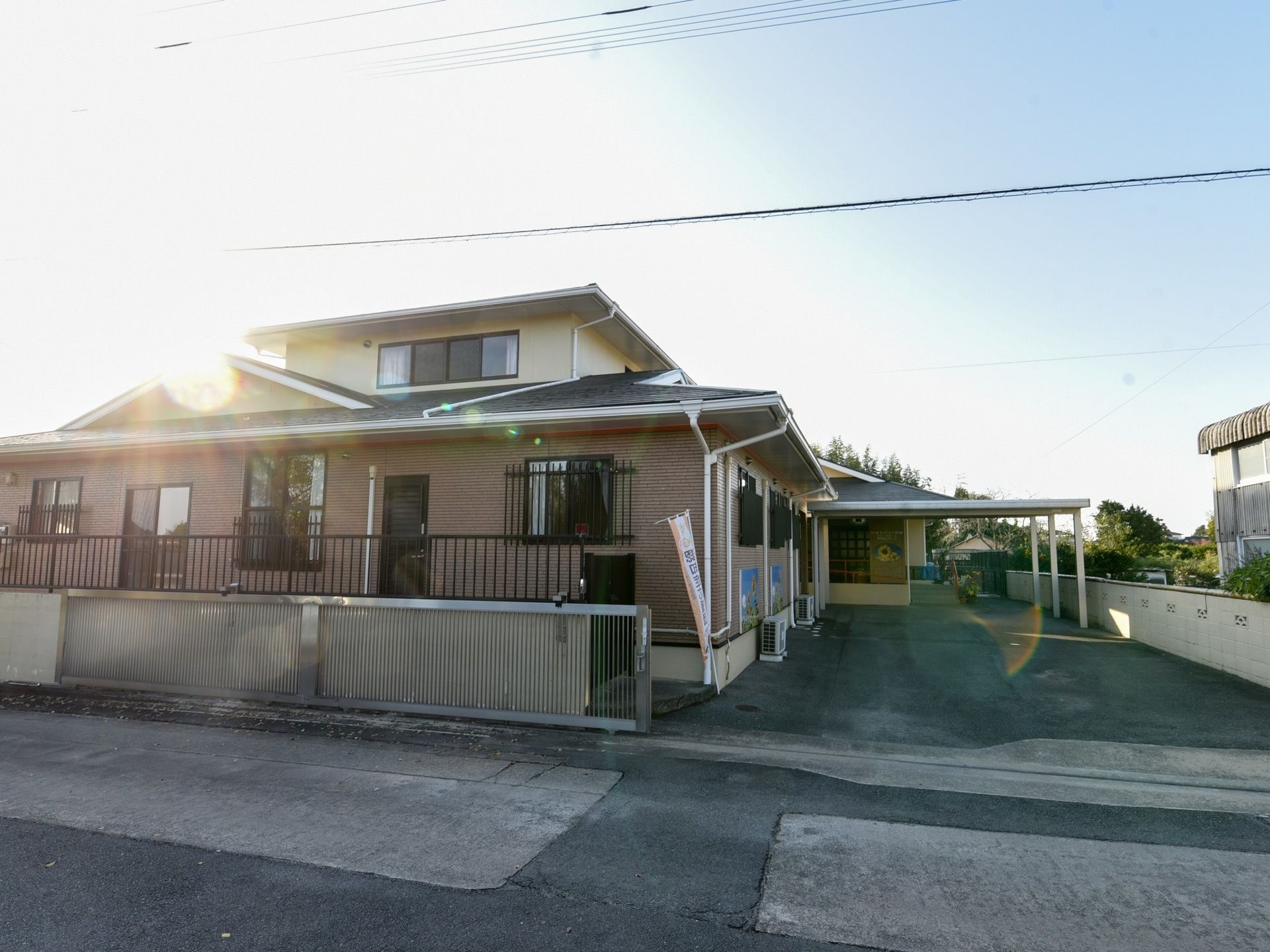 ベージュの外壁の2階建てで、黒い三角の屋根になっている。窓には格子がついていて、下にはエアコンの室外機が置かれている。
