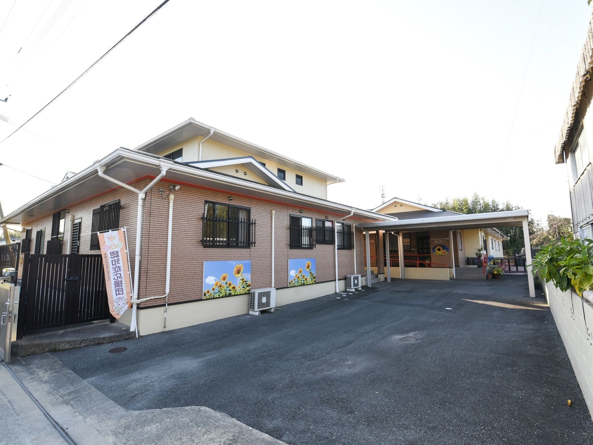 ブラウングレーの外壁に三角の屋根が乗った建物である。外壁には施設名を象ったひまわりの花の絵が描かれている。