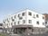 ３階建ての建物を左斜め前から撮影。１階部分は茶、２階と３階は白、玄関部分には車寄せが付いている。