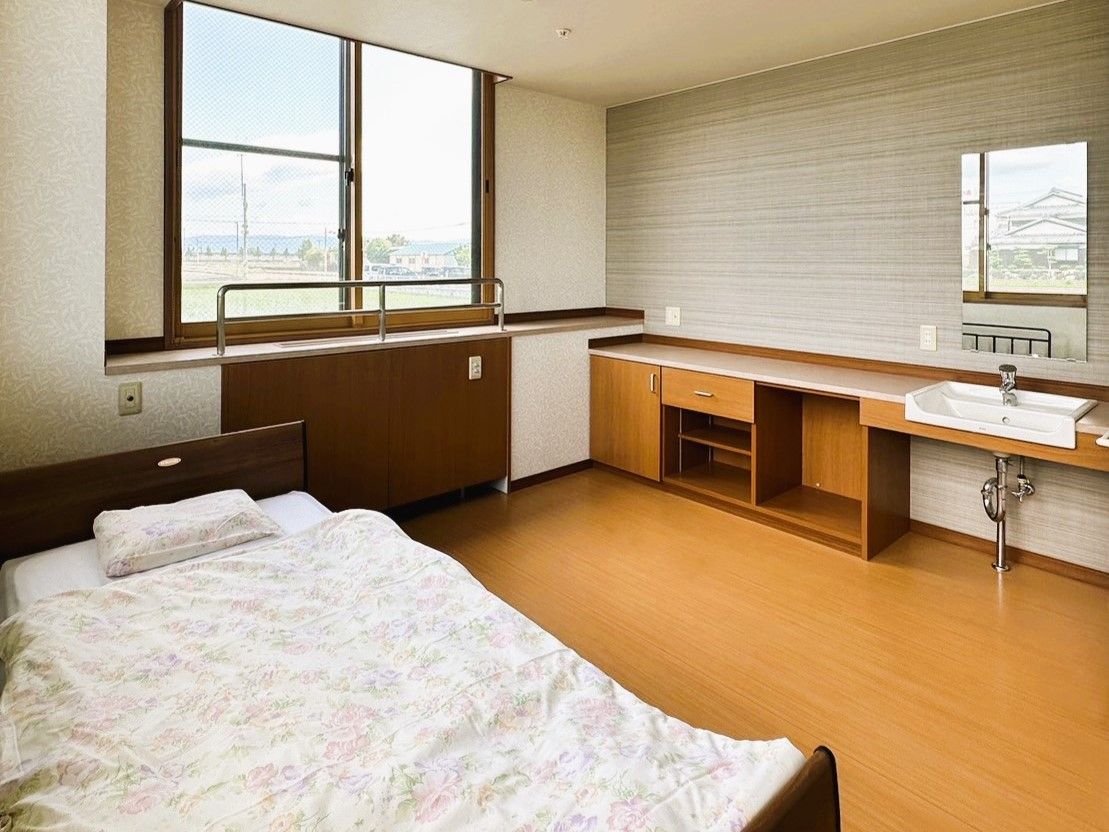 手前にトイレが見え得ている個室の様子。やわらかい照明と収納棚、手すりがある