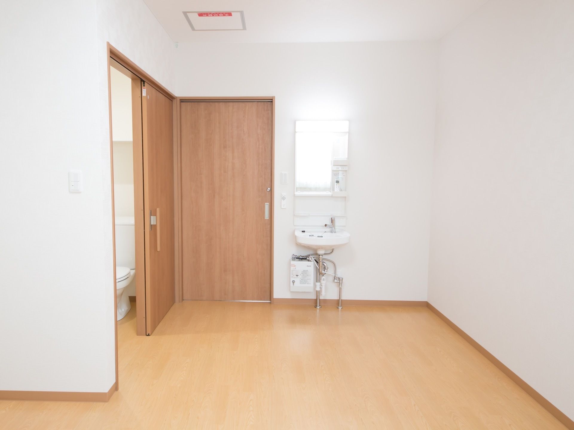 居室の入口扉の横に、引き戸のドアがあり中はトイレになっている。入口入って左手には洗面台があり、壁に鏡がある。