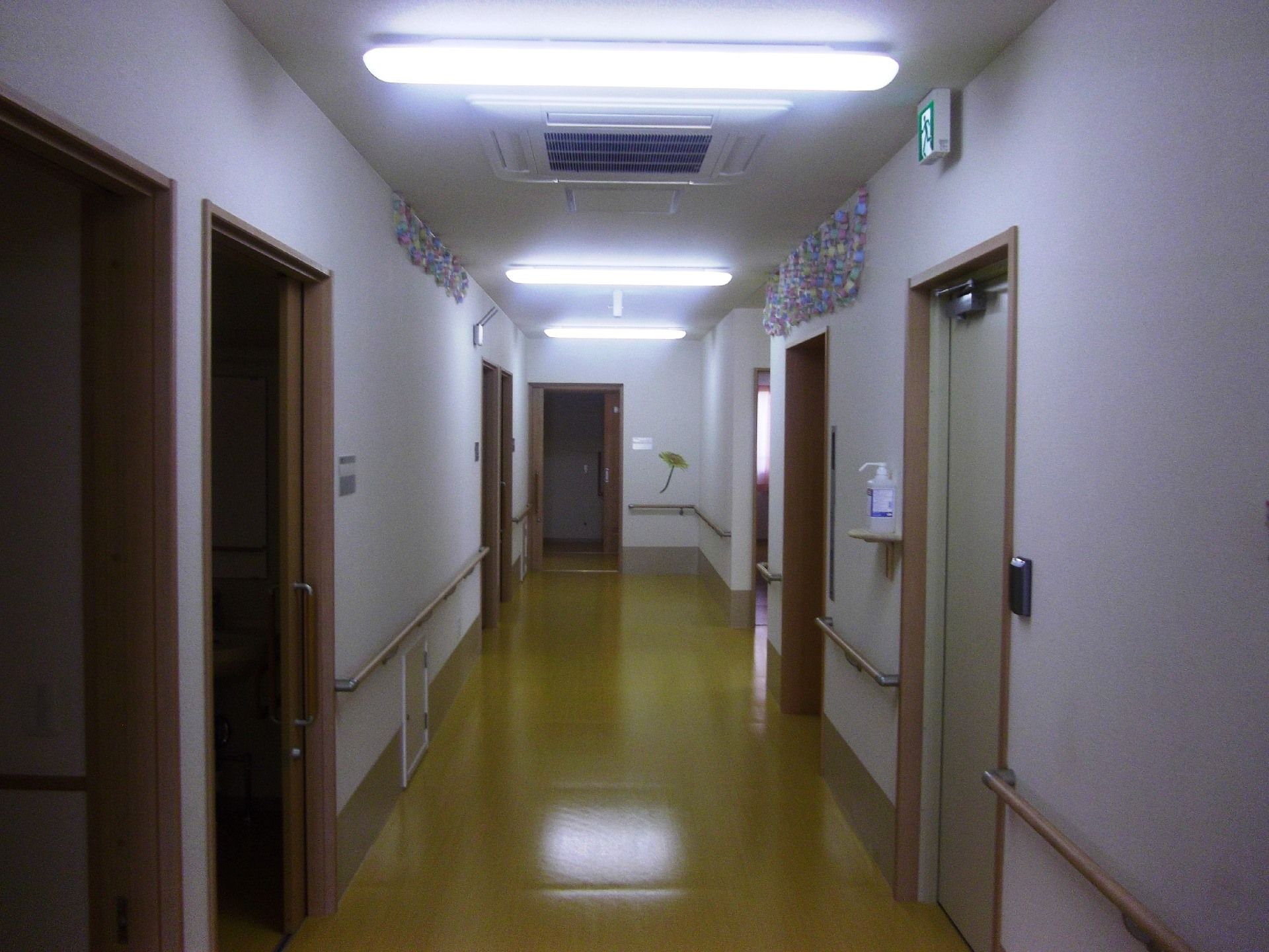 白い壁に茶色のドア枠が映える。右手手前の部屋の入り口には消毒液もセットされている。