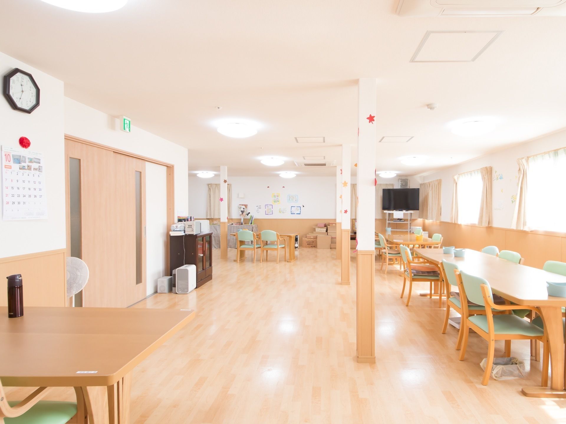 窓からの光で明るく、広いスペースである。白い壁で、腰から下の壁面と床は木目調である。端にテーブルセットが並び、ドアはスライド式である。