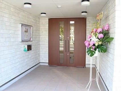 玄関は少し奥に入っているため雨でも濡れない。豪華なお祝いの花が置かれている。