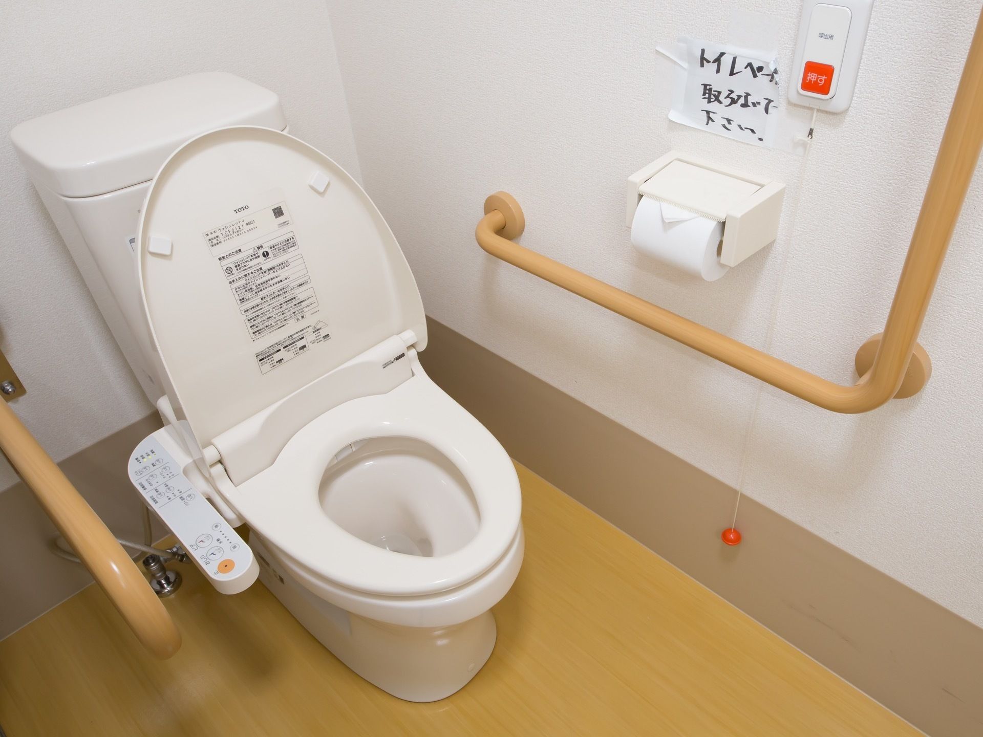 トイレの壁には縦方向と横方向に木目調の手すりが設置されている。目立つ色合いで手に取りやすく、また手触りも良い。