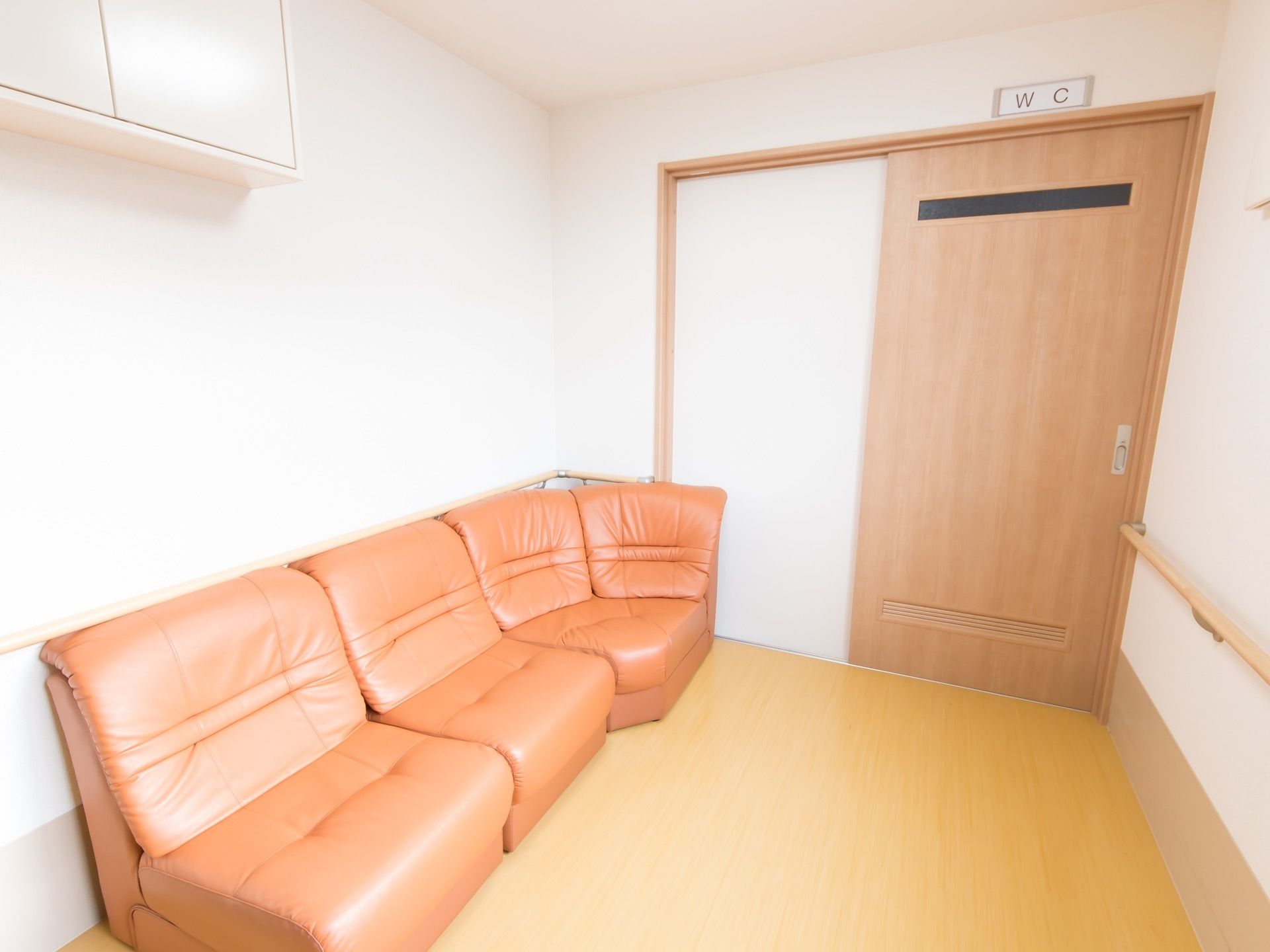 トイレの前に休憩スペースがあり、茶色のソファが置かれている。壁の上部には、天袋が設置されている。反対側の壁には手すりが取りつけられている。