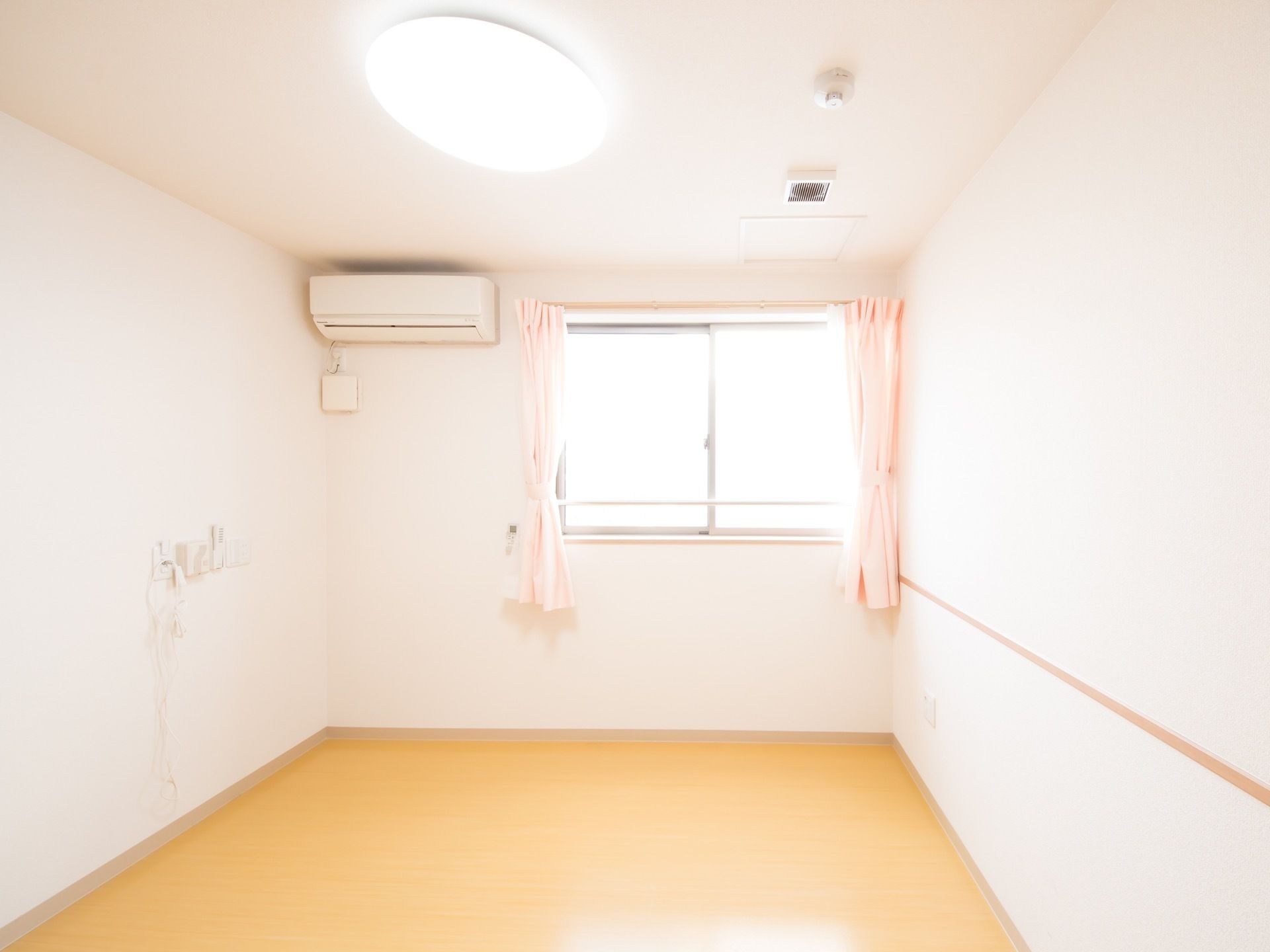 居室に腰窓があり、レースとピンク色の厚地のカーテンが掛っている。入居者様の好みで自由に採光を調節することができる。