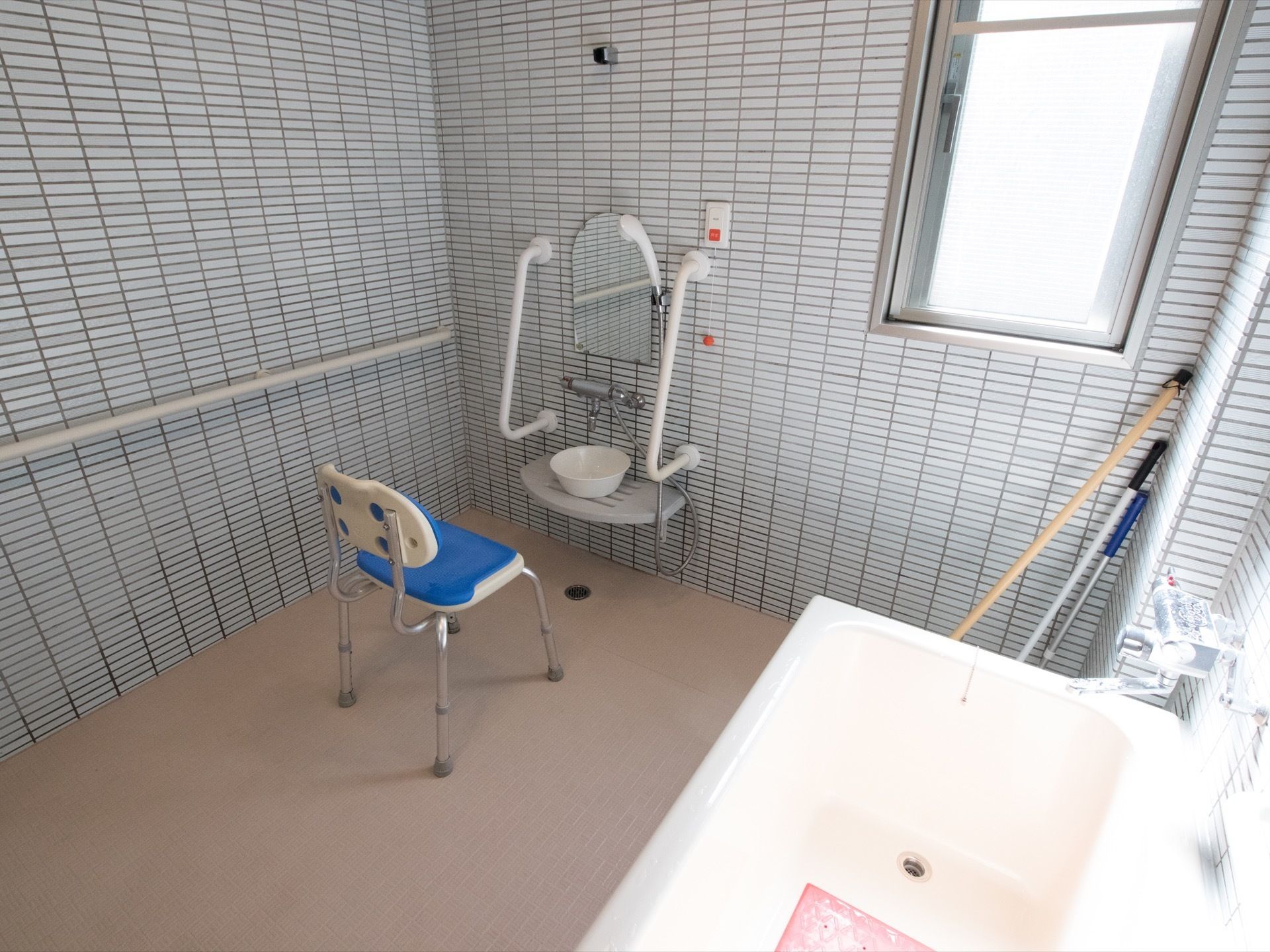 青色のシャワーチェアが洗い場に置かれている。洗い場には鏡が取りつけられており、その両側に手すりが設置されている。