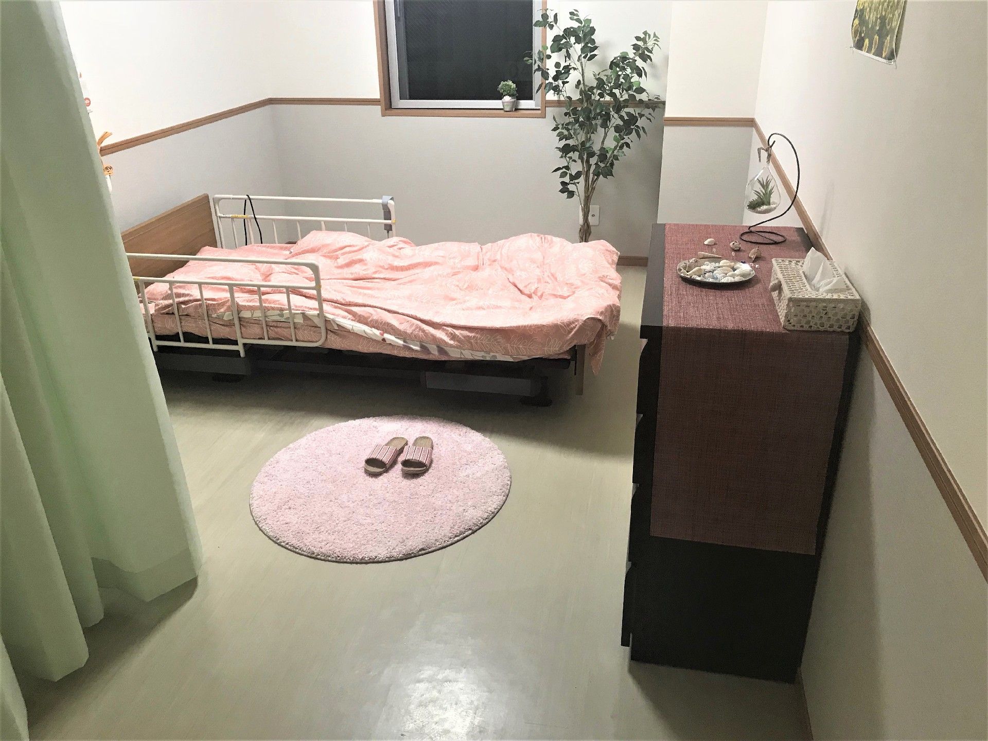 木製の小さい棚とベッドが置かれた居室。ベッド周りはピンクで統一されている。