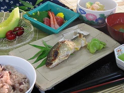 メロンやチェリーなどの果物やアユの塩焼き、エビなどの刺身、赤飯と、ごちそうが並んだ食卓。