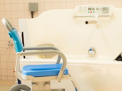 白い機械浴とブルーの浴室用車いす。浴室全体はピンクのタイルが貼られている。