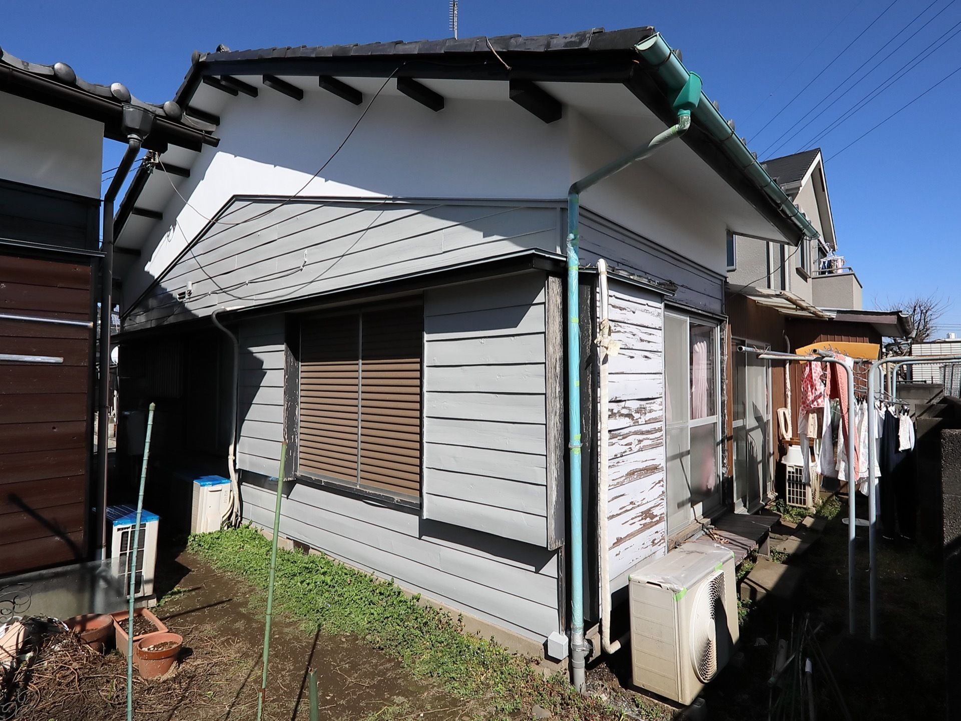 1階平屋建ての建物で、窓には雨戸が閉められている。窓の前には洗濯物干しが複数設置され、衣類が干されている。