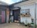 施設の隣には住宅が建てられており、間にはブロック塀が建てられている。玄関ドアの両脇にはプランターなどに植えられた植物が飾られている。