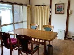 カーテンやテーブルなどはピンク色で統一されている。窓の上部にはエアコンや扇風機などが設置されている。