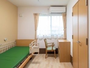 収納付きの広い部屋には介護用ベッドやエアコン、デスクにいすもある。
