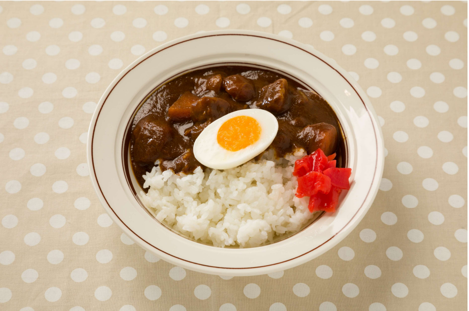 黒いお盆の上にご飯、豆腐とわかめの味噌汁、ちくわと糸こんにゃく等の煮物、キュウリの和え物等が並べられている。