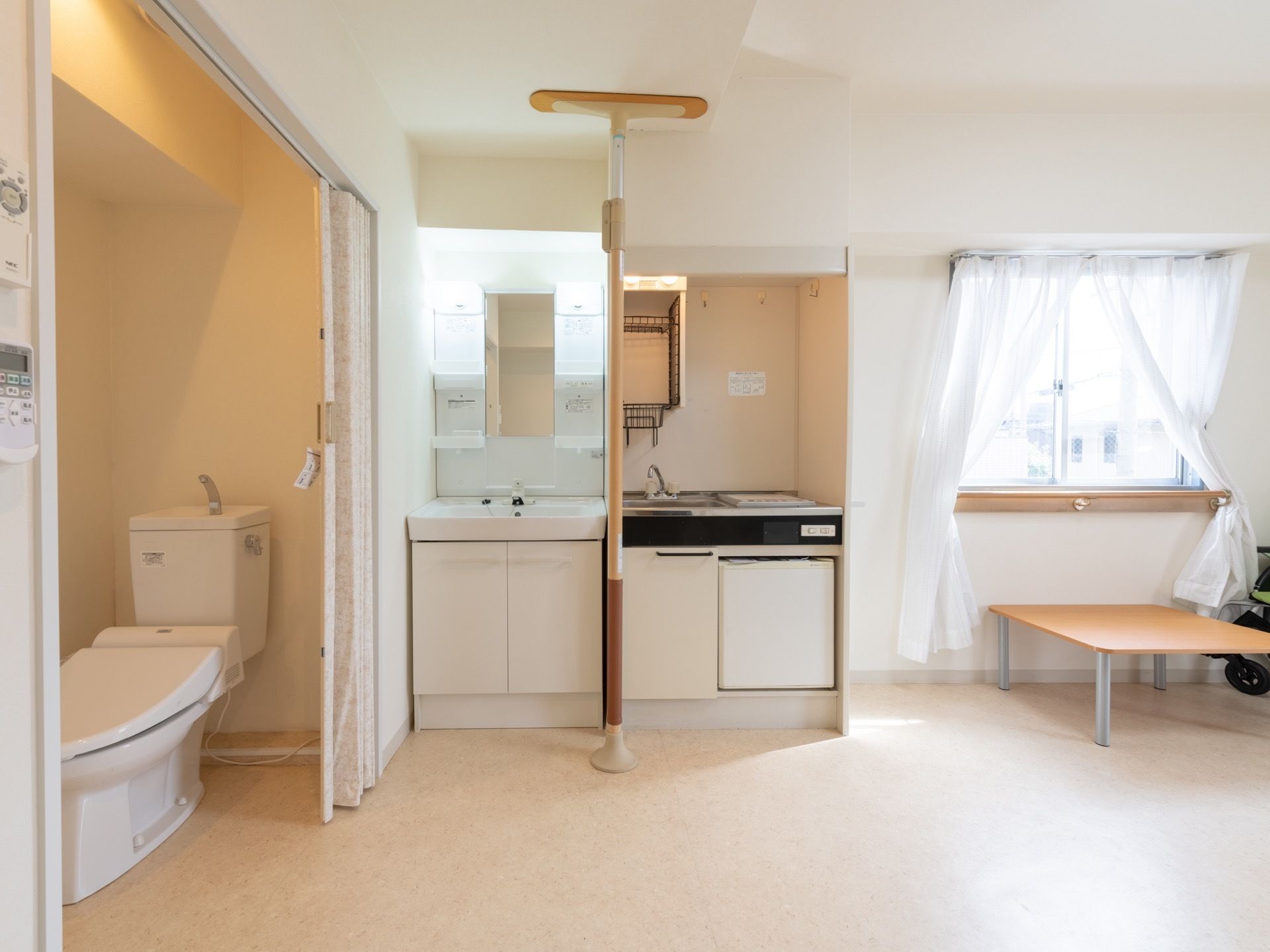 居室は白とベージュを基調としている。トイレの扉はアコーディオンカーテンになっている。洗面台と流し台が隣接している。
