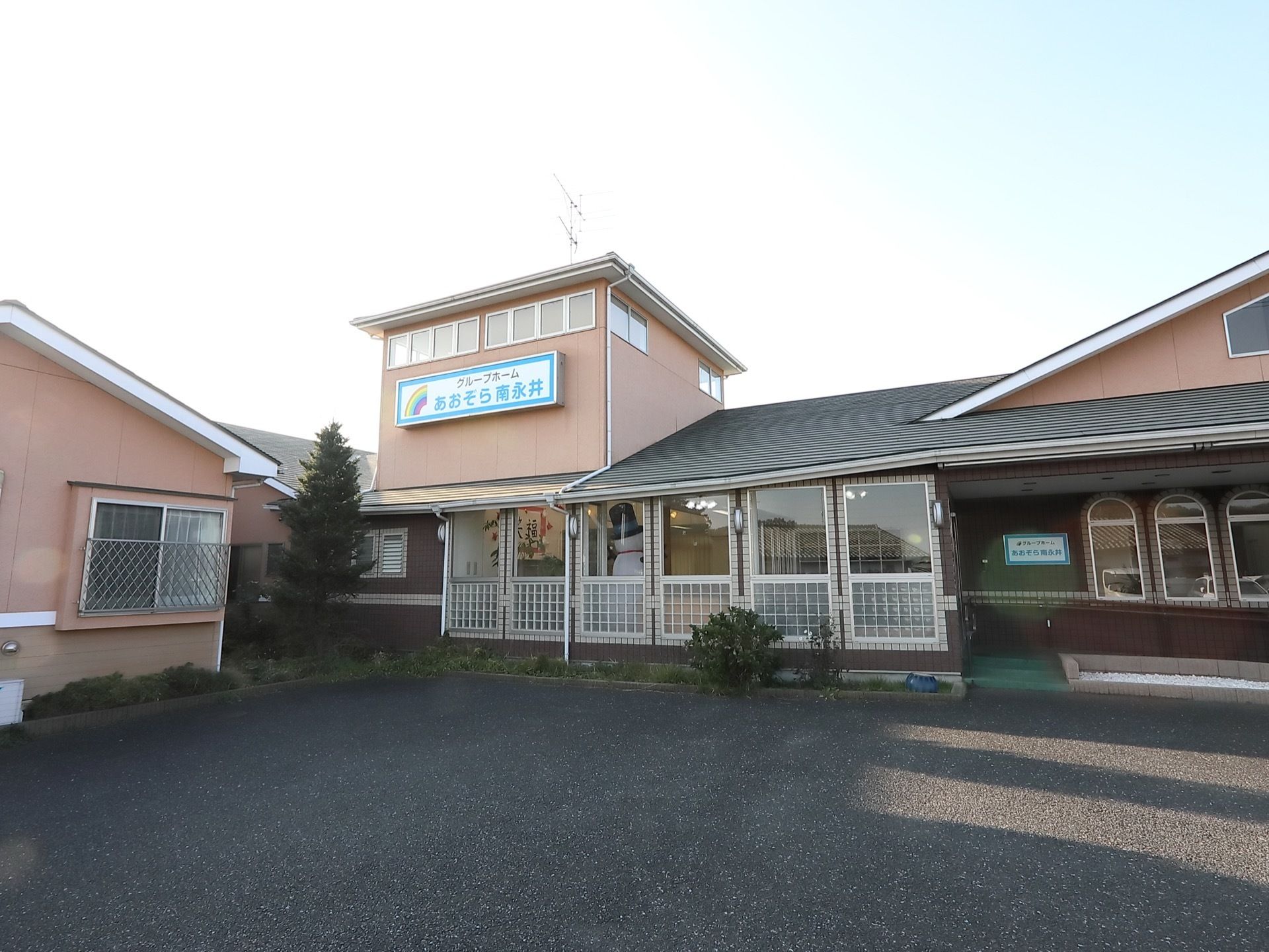 落ち着いたピンクの壁とグレーの屋根のデザイン性のある建物。壁には大きな看板があり、施設名が書かれている。
