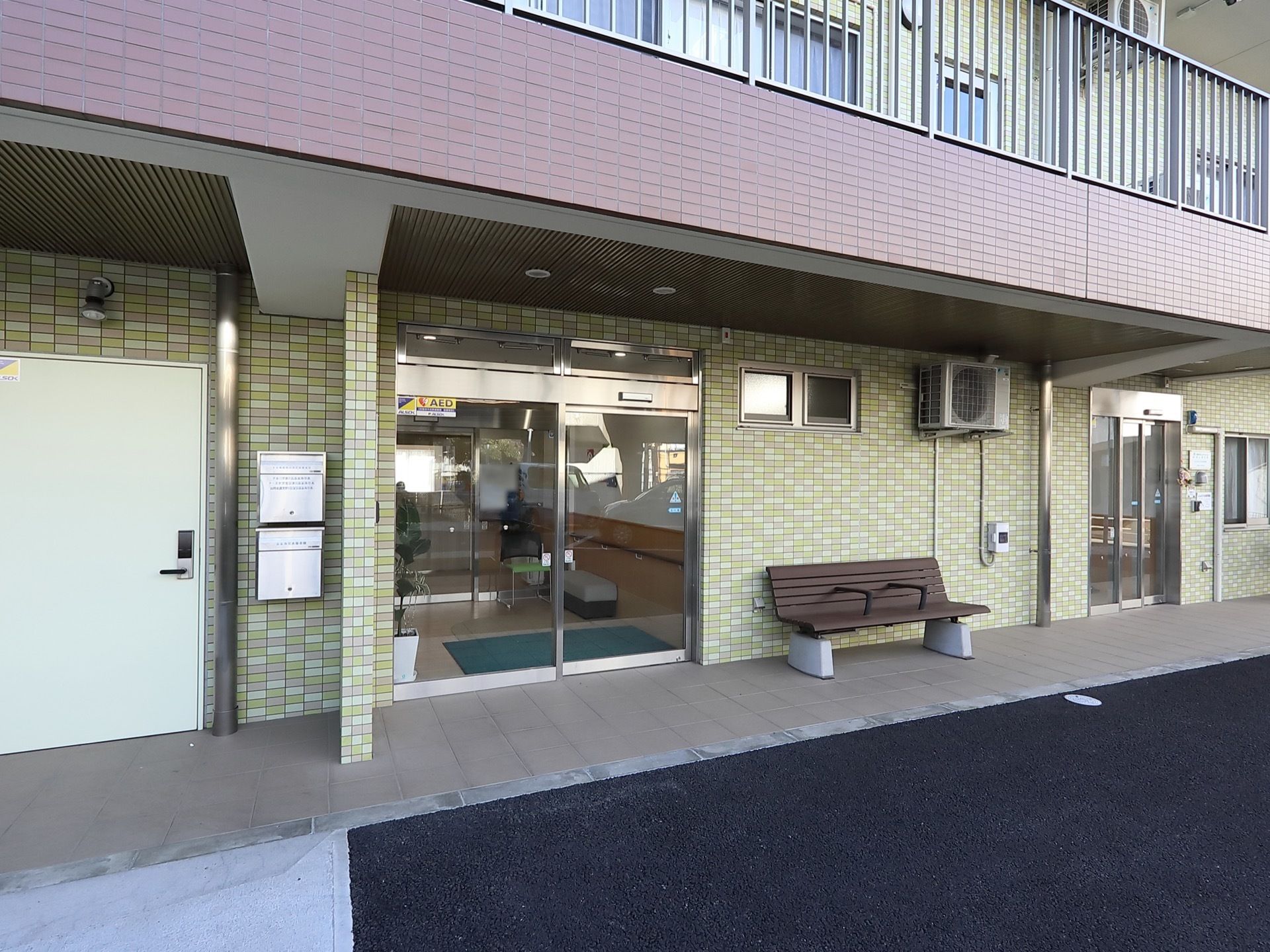 全面がガラスの自動ドアが設置されている。ドアの左側壁に新聞受けが2個取りつけられている。右側にやや細めの同じく自動ドアの入り口がある。