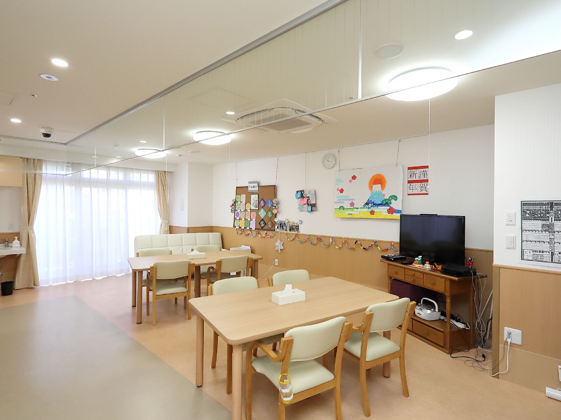 優しい色合いの４人掛けテーブルやソファが配置されている、明るく開放的な食堂