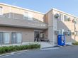ピンクの外壁の２階建ての施設である。壁に大きく施設名が表示されている。施設前には自動販売機が置かれている。