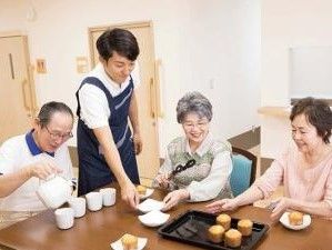 ティータイムにテーブルを囲んでおやつを食べようとしている入居者と準備を手伝うスタッフ。