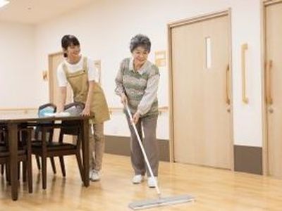 モップで床掃除をしている入居者をやさしく見守るスタッフの様子。