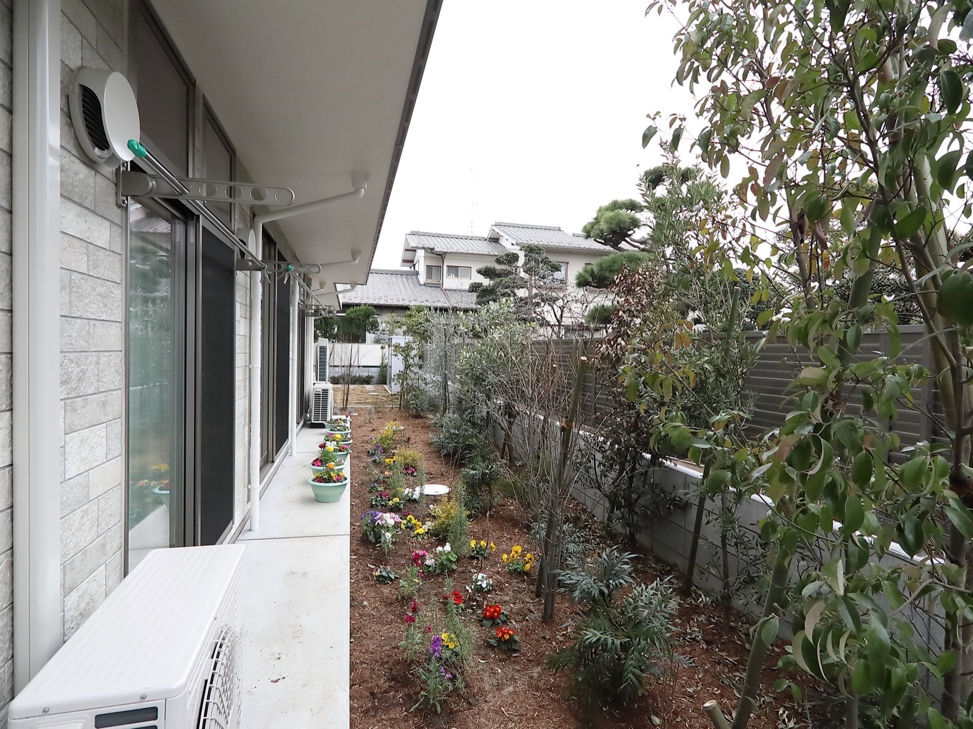 施設の建物裏には、数種類の花や庭木が植えられた裏庭が設けられている。物干しがそれぞれの居室の窓際に設置されている。