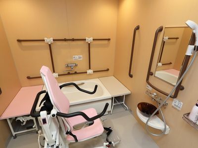 清潔感漂う個浴室である。複数の手すりや移乗台が完備されており、リフト付きシャワーキャリーが用意されている。