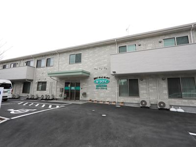 施設は２階建ての建物である。２階の居室には、バルコニーが設置されている。広い駐車場が建物の前に設けられている。