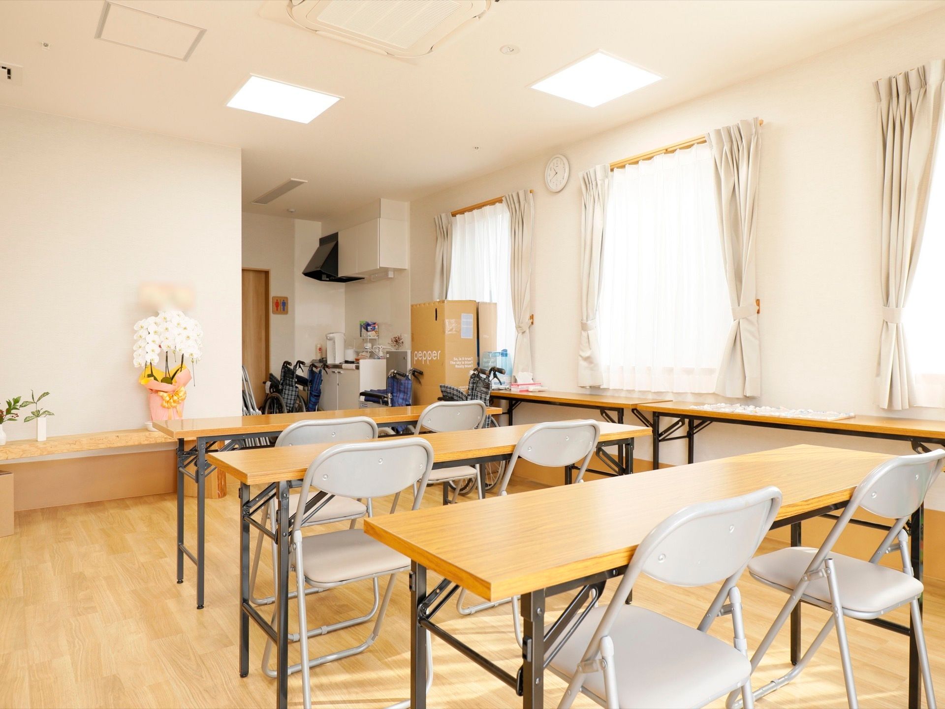 白い壁が美しく明るい会議室である。長テーブルが３台と折り畳み式のパイプ椅子が６脚並んでいる。奥にはキッチンがある。