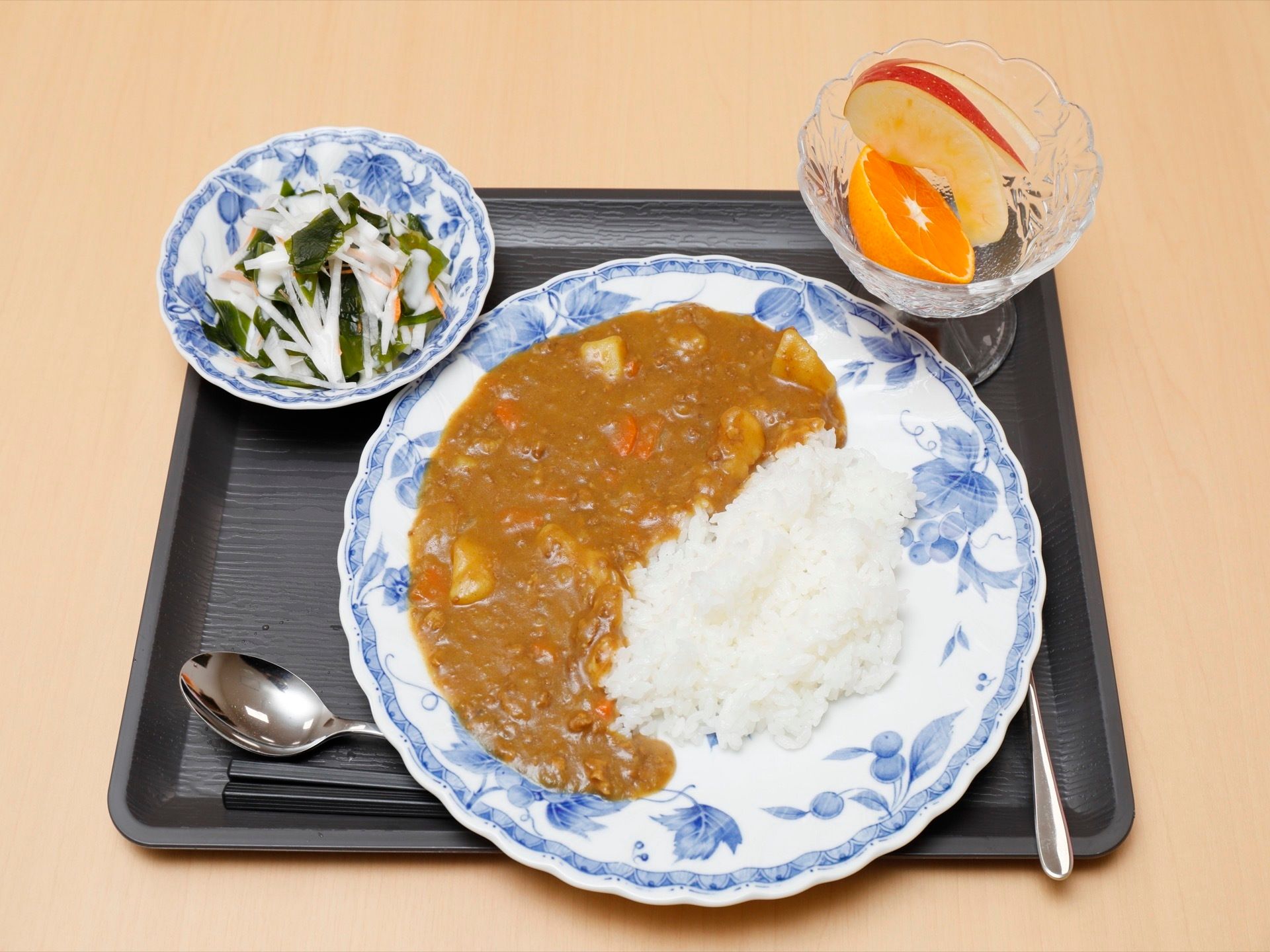 ある日の給食である。野菜たっぷりカレーライスやわかめと大根のサラダ、みかん1/2、うさぎに見立ててカットしたりんご１切れである。