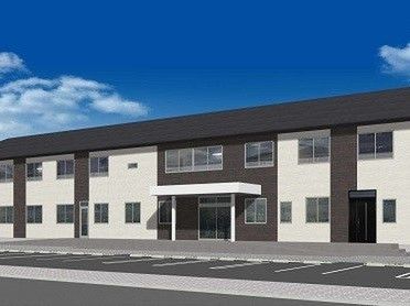 2階建ての建物。白い外壁にグレーのラインが入っていて屋根もグレー。敷地内には広い駐車スペースがある。