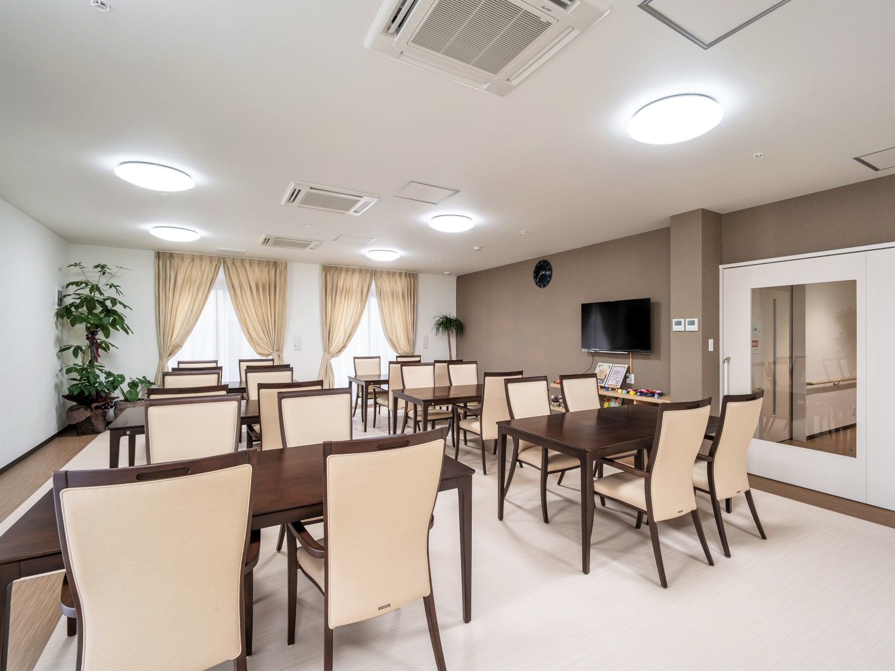 大型の壁掛けテレビが設置された食堂には４人掛けのダイニングテーブルが複数置かれている。