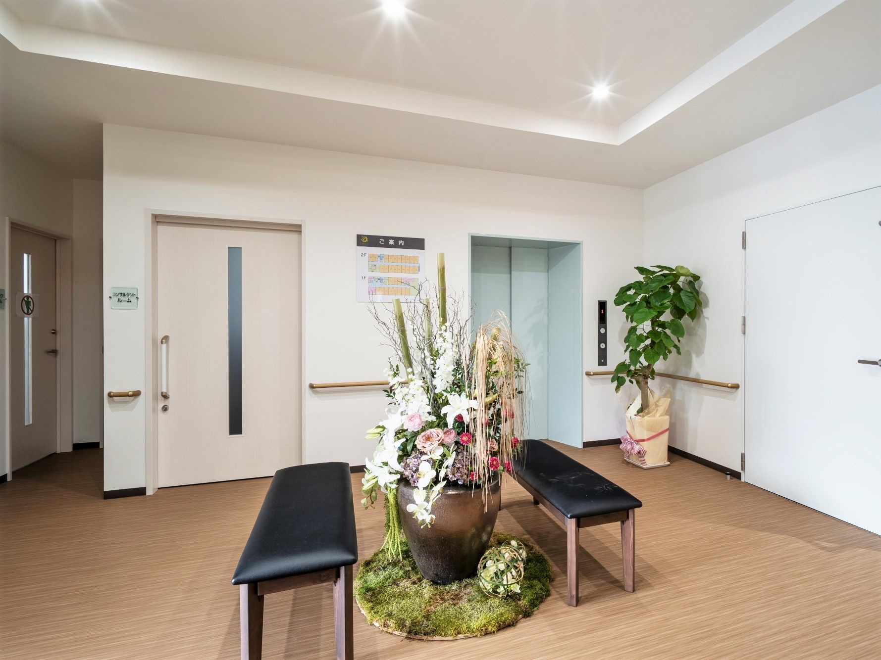 エレベーターの前には観葉植物があり、二つのベンチと大きなフラワーアレンジメントも置かれている。
