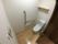 小さな額が飾られたトイレはフローリングで引き戸、エル字型の手すりや呼び出しボタンもある。