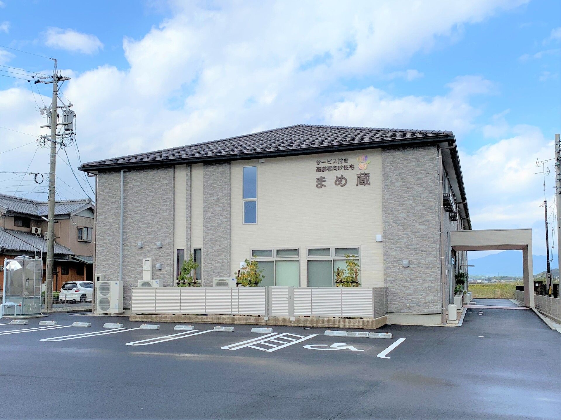 2階建ての建物を側面から見た様子。側面の外壁には住宅の名前が書かれていて、駐車場もある。