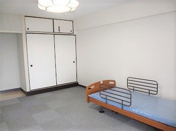 クッションフロアが敷かれた居室には青いマットレスが敷かれたベッドがあり、押し入れ風の収納スペースもある。