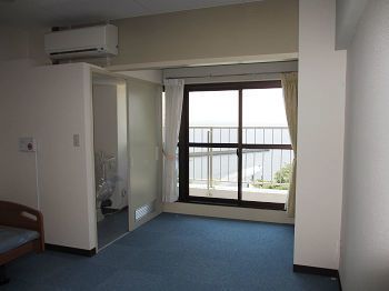 左手に大きな収納スペースとエアコンが設置された居室。窓が大きく、ベランダが付き、海が見える。