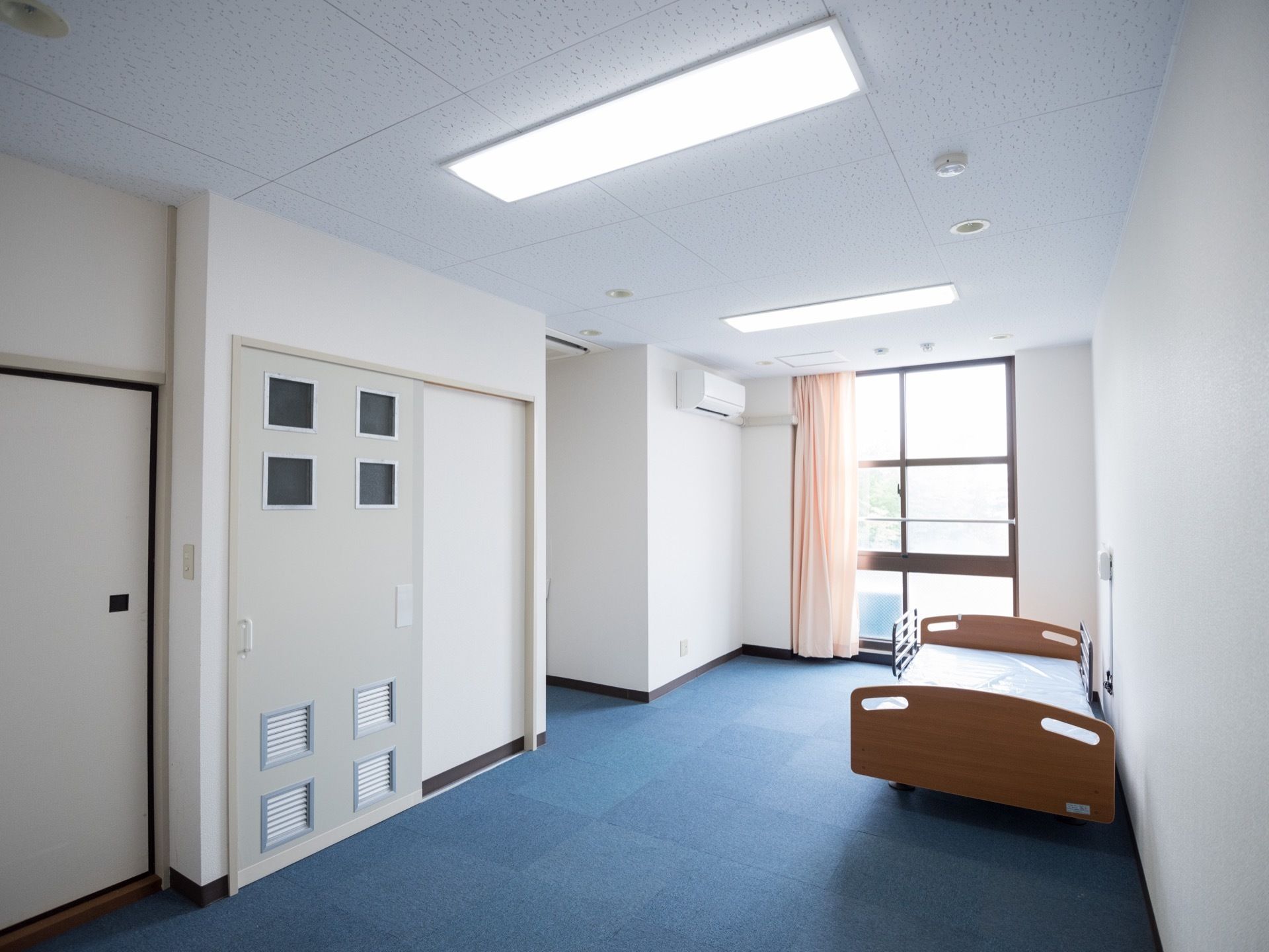 広々として清潔感のある居室の奥には大きな窓があり、室内に外の日の光が入るようになっている。天井が高く開放感のある造り。