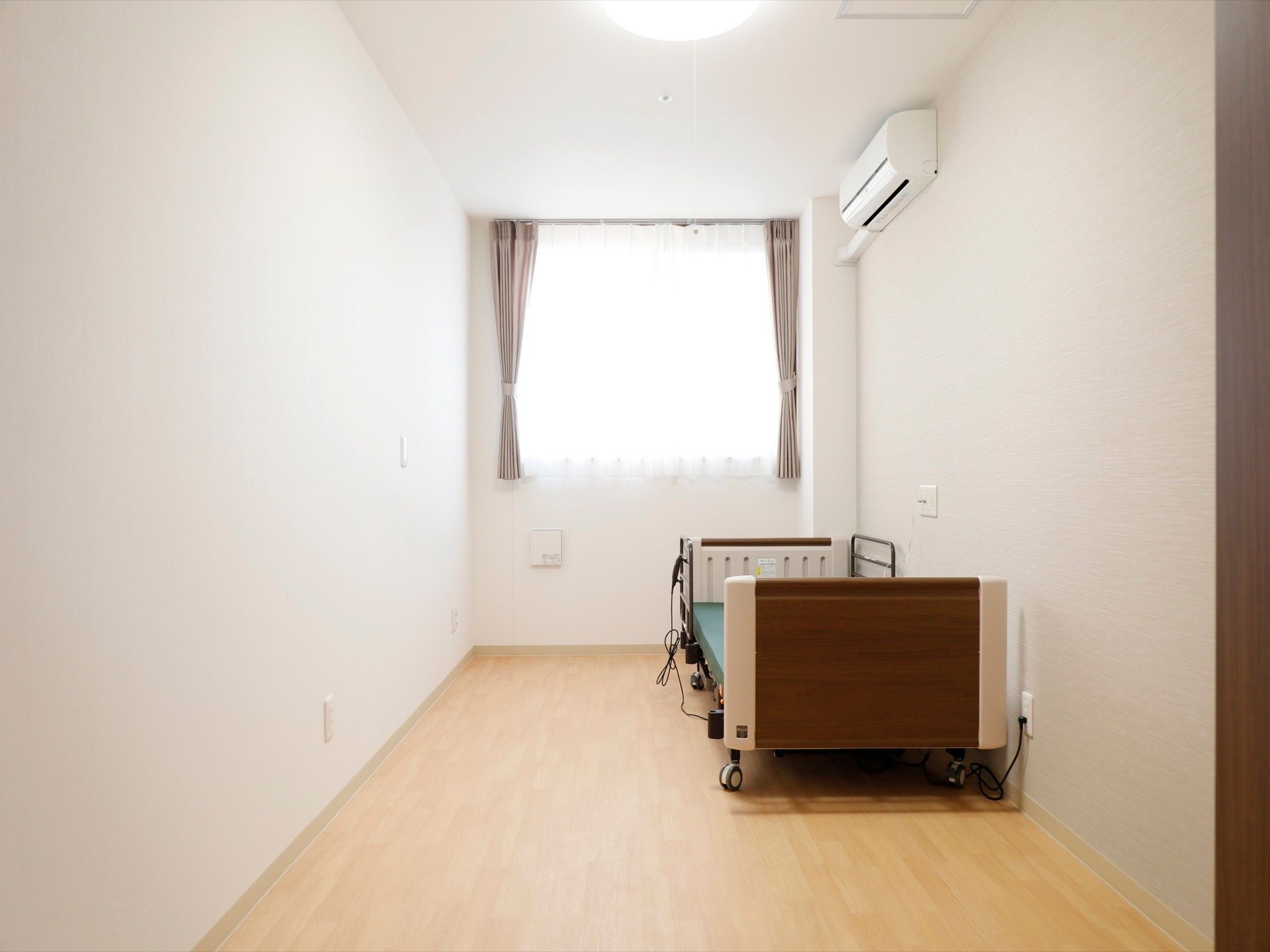 居室には快適に過ごせるように、電動のベッドやエアコンが完備されている。窓から日が差し、明るい部屋である。