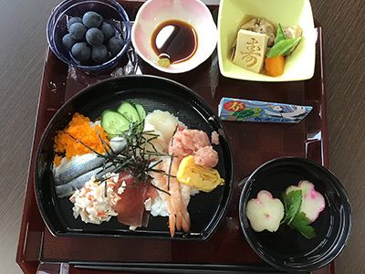 海老やまぐろやほたてなどをトッピングした海鮮丼と野菜の煮物と吸い物とぶどうのデザート