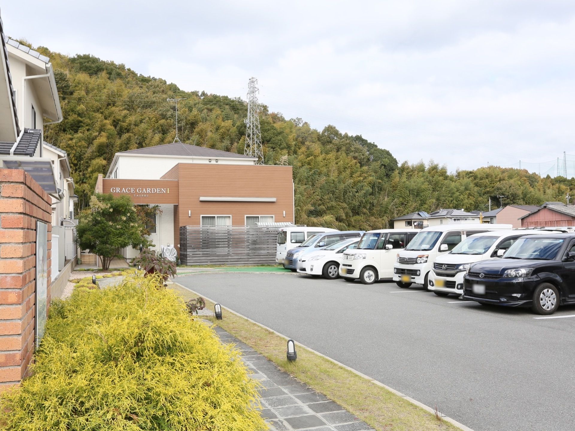 ２階建てのグループホーム。施設目の前にあるアスファルトで舗装された駐車場には、複数台の車が停められている。