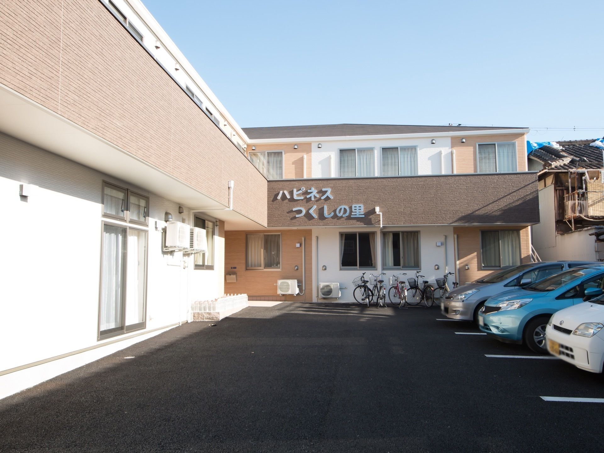 L字型の二階建ての建物がある。建物の手前は舗装された駐車場になっている。外壁には大きな文字で施設名が書かれている。
