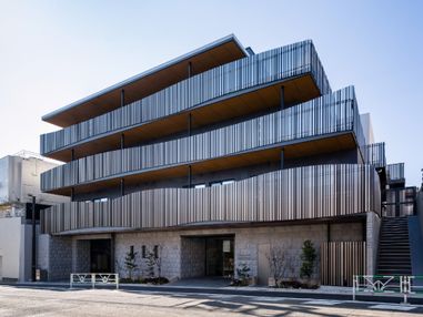 ４階建ての建物。玄関周辺には木が植えられ、駐車スペースもある。